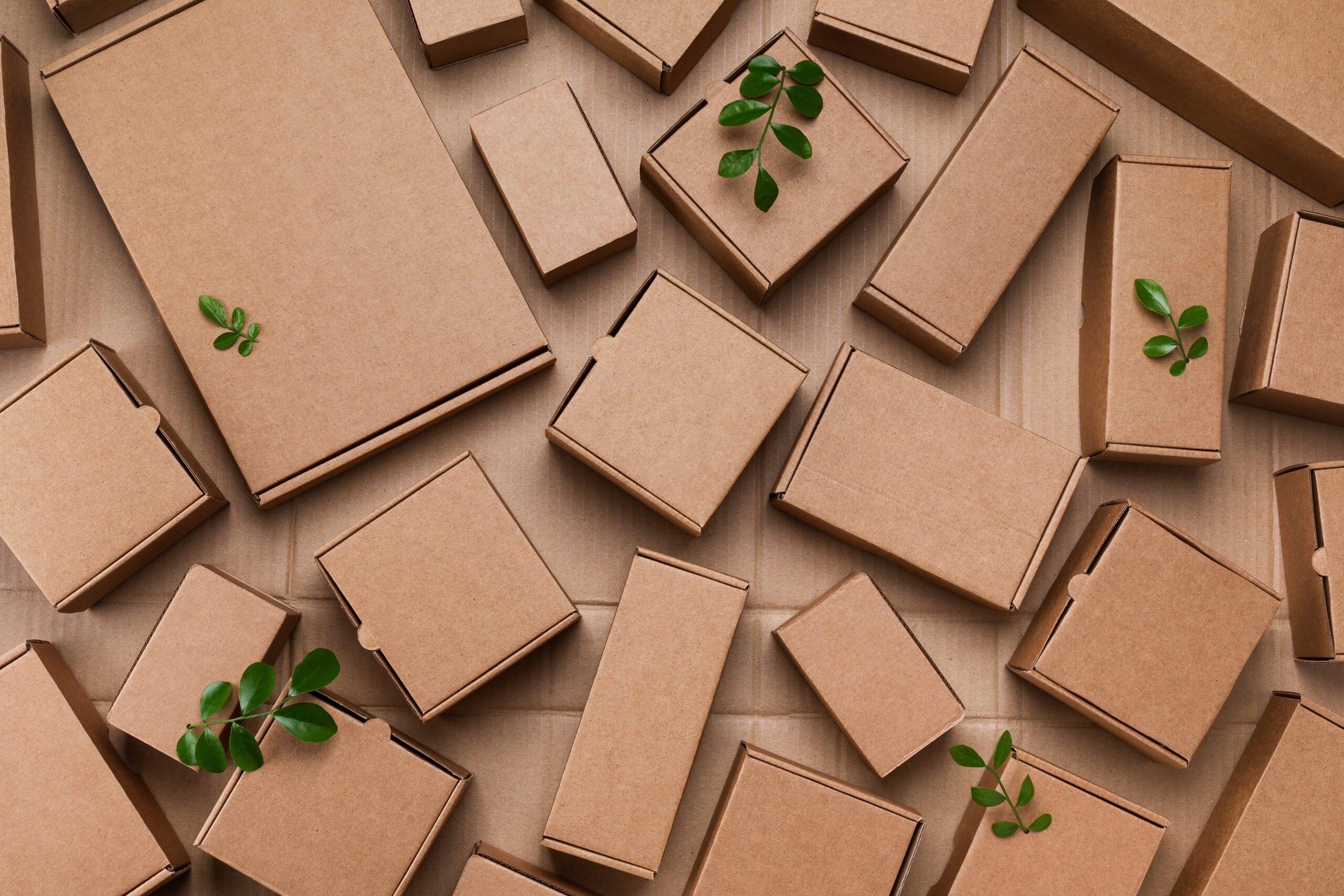 Heap Of Cardboard Boxes From Natural Recyclable Materials With G Heap of cardboard boxes from natural recyclable materials with green leaves sprout top view. Responsible consumption, eco friendly packaging, zero waste concept.